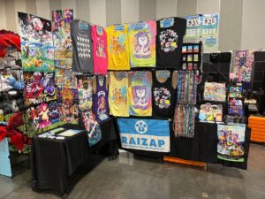 A photograph of RAIZAP by Chu's convention table setup at Another Furry Con 2024.