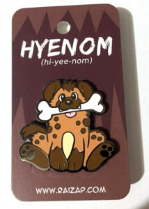 HyeNOM enamel pin featuring a cute spotted hyena with a bone in its mouth